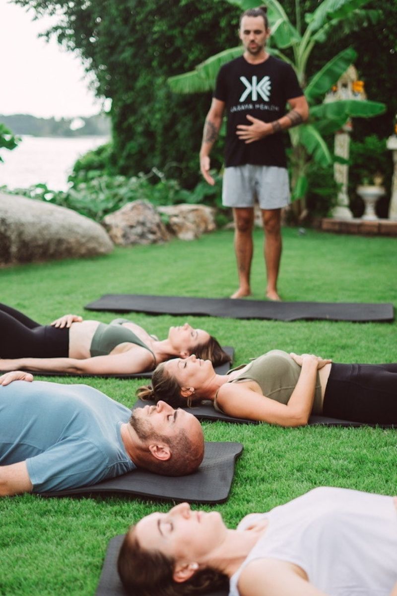 Group of people lying on mats with a instructor standing and talking outdoors.