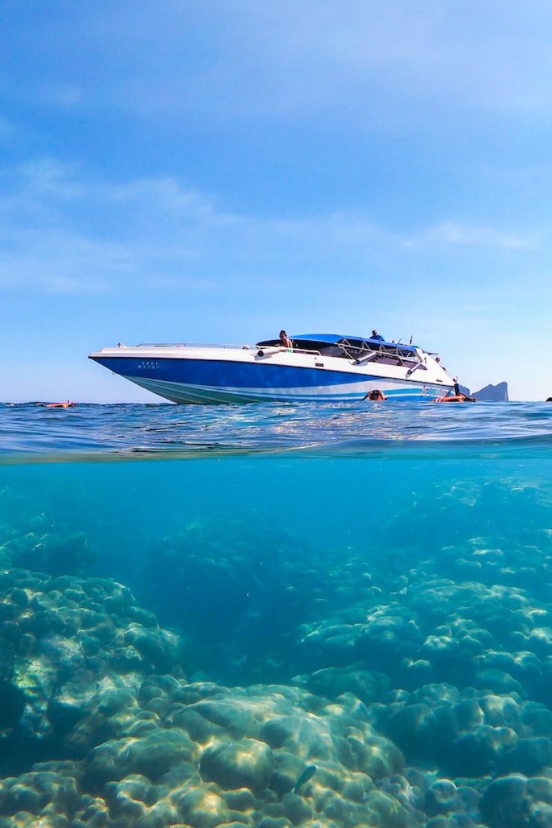 Boat on the water with a clear blue sky and underwater view of rocks and sand.