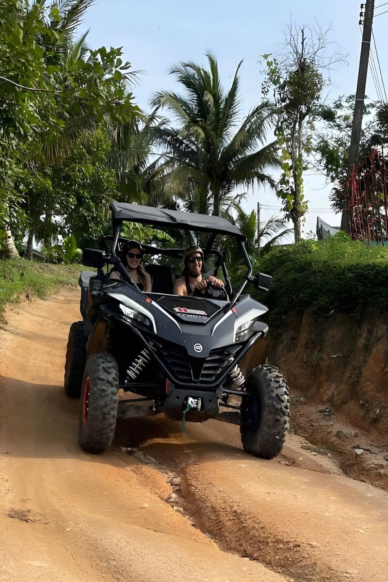 Off-road vehicle with two people driving on a dirt road surrounded by trees