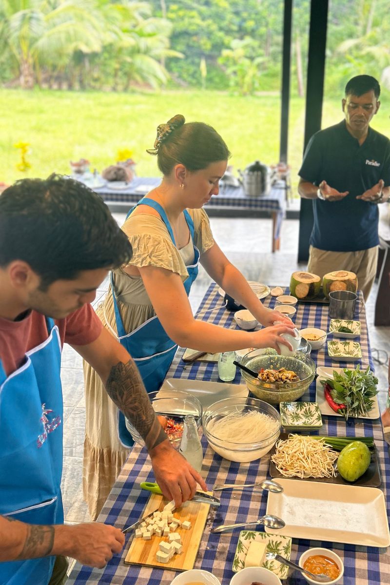People preparing food at a table with a checkered tablecloth outdoors.