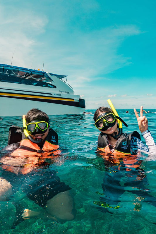 Two people snorkeling in clear blue water with a boat in the background.