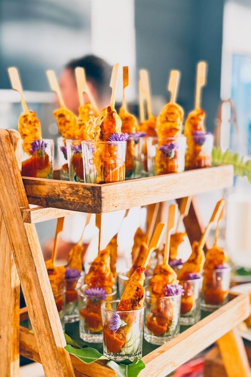 Dessert skewers with purple flowers in small cups on a wooden stand.