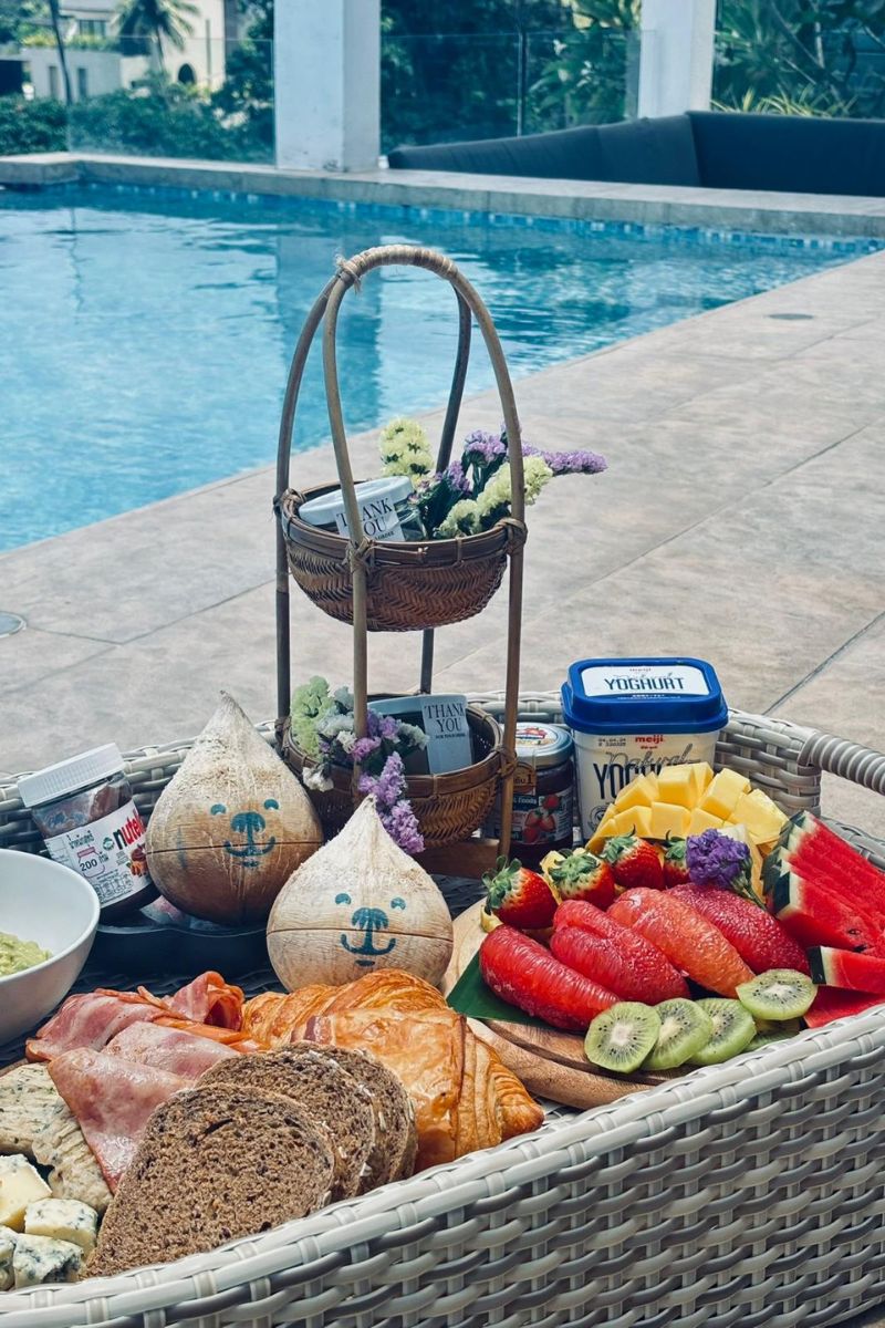 Outdoor picnic setup with fruits, bread, and drinks by a poolside.