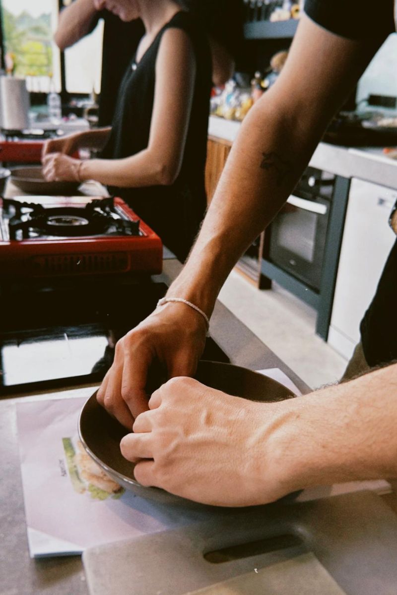 Two people preparing food in a kitchen, with one person holding a pan.
