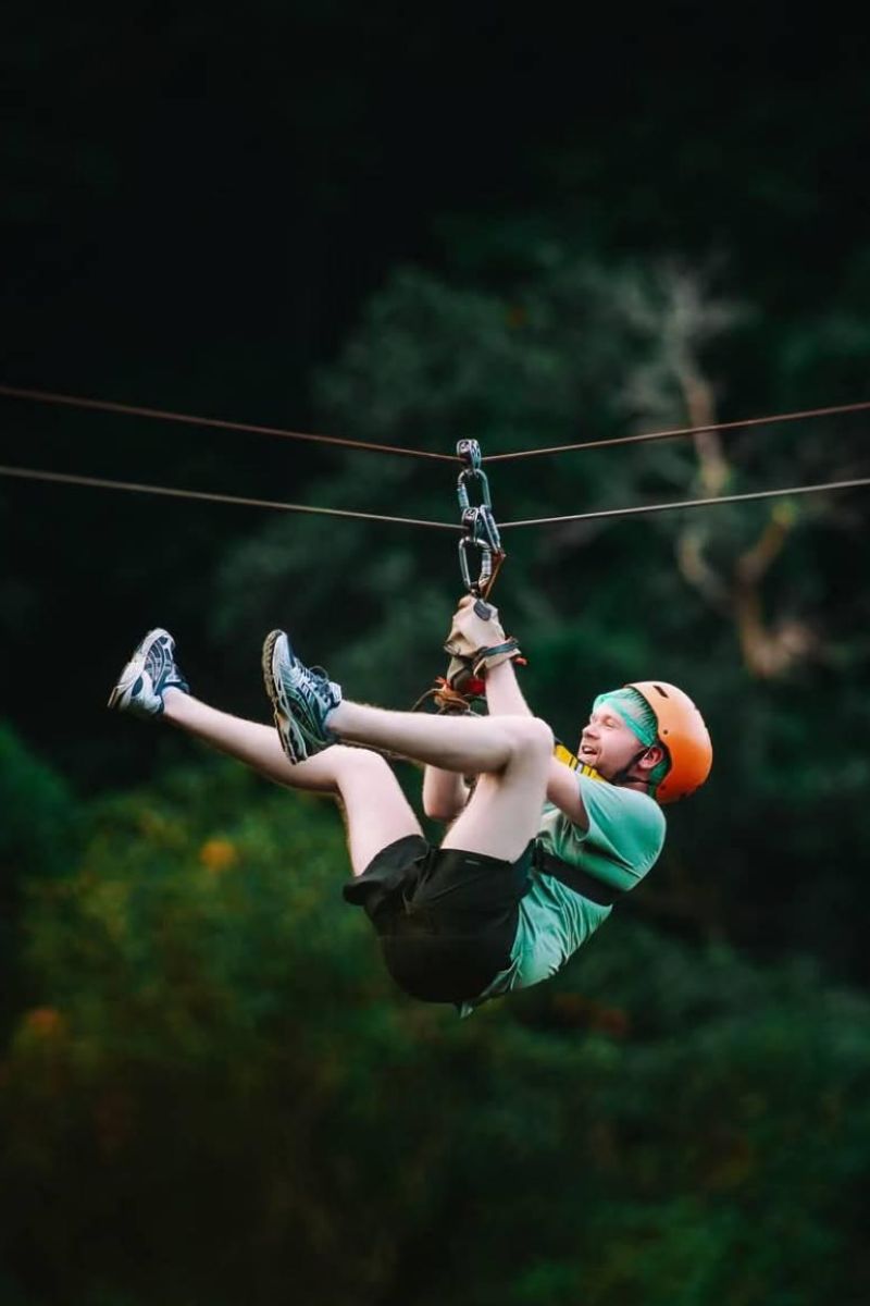 Person zip-lining through a forest with a helmet on