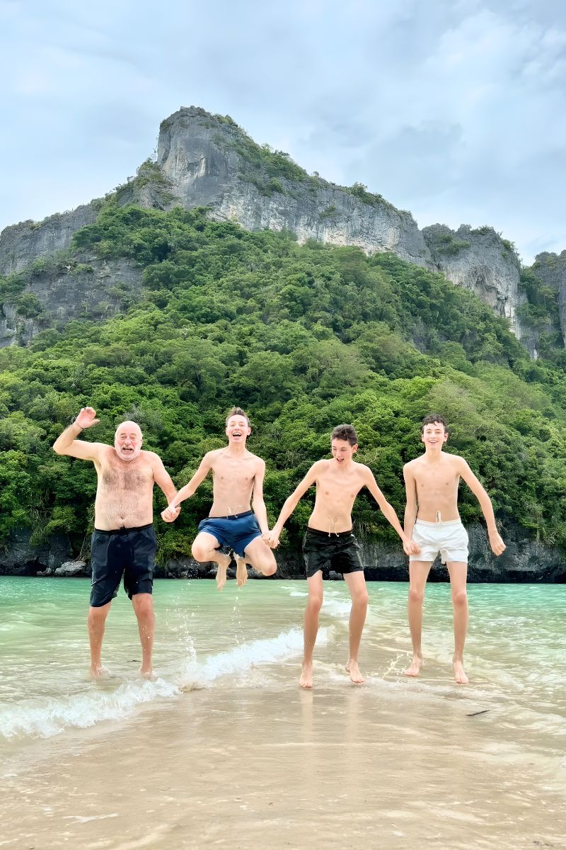 Four men standing in shallow water on a beach with a mountainous island in the background.