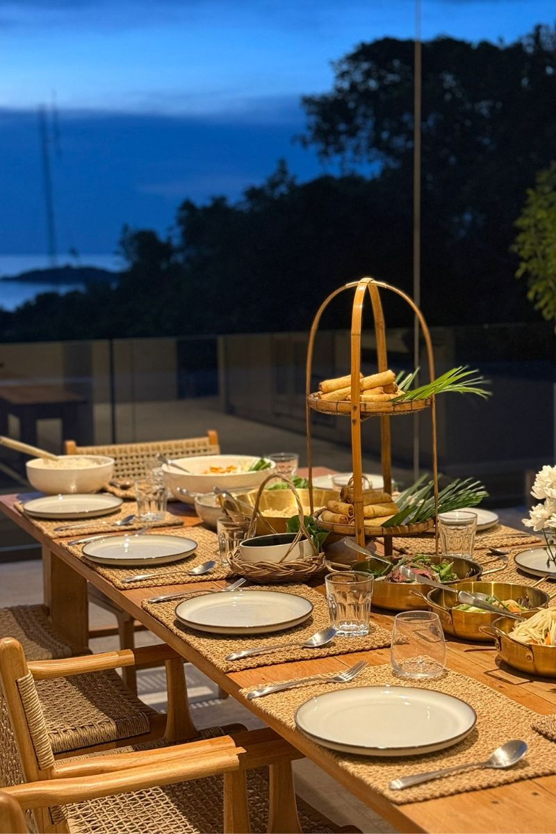 Dining table set for a meal with plates, glasses, and cutlery on a wooden table outdoors at dusk.