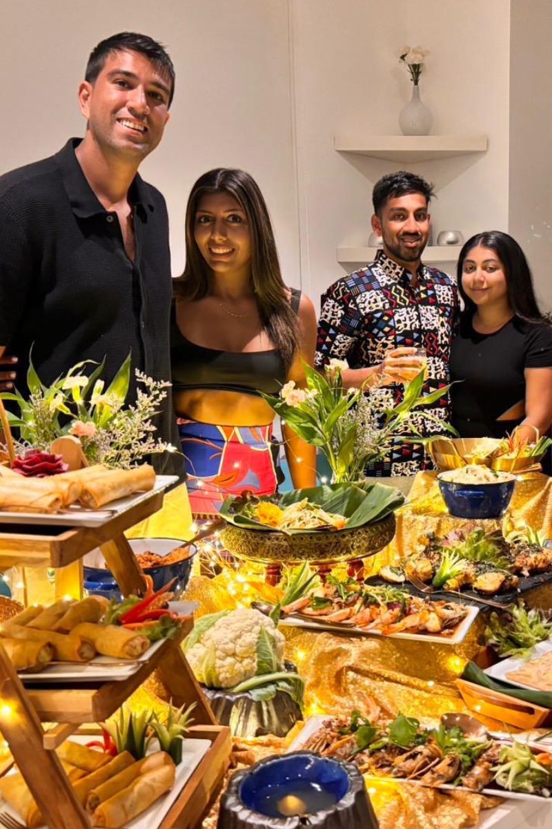 Group of people posing in front of a large spread of food in a kitchen.