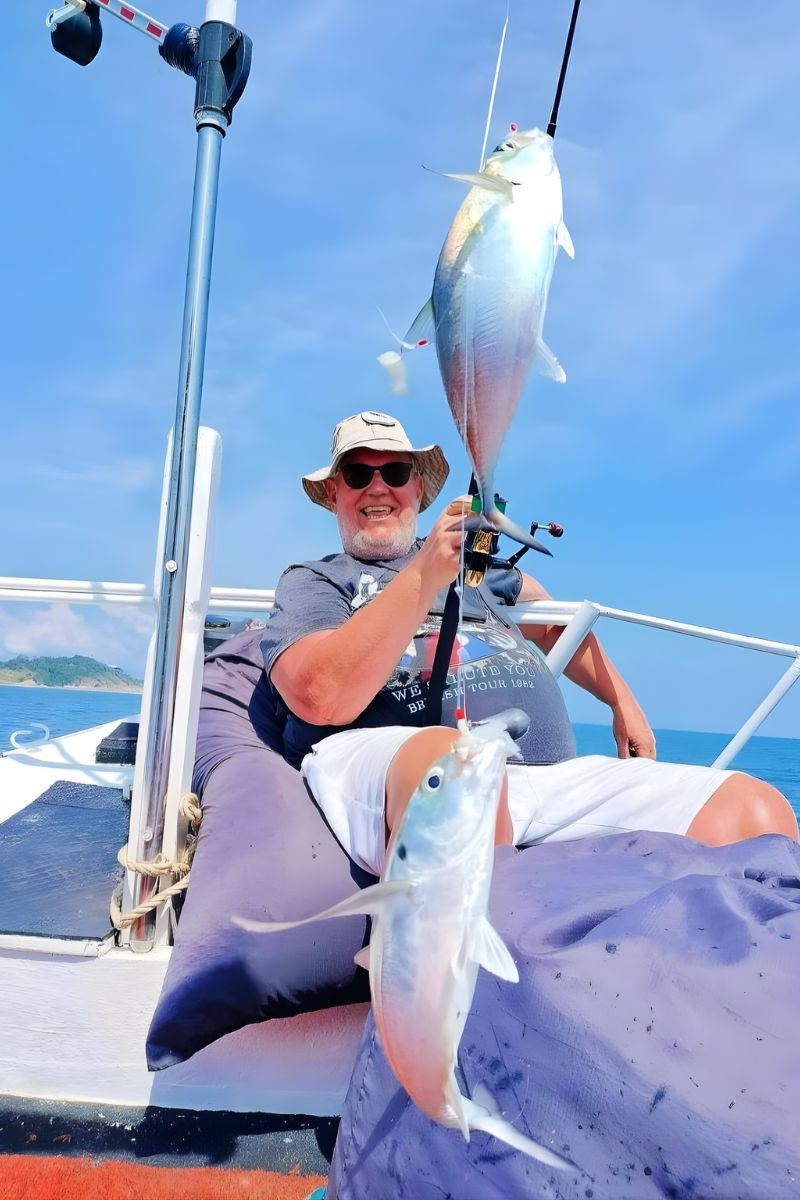 Person on a boat holding a fish caught from a line against a clear blue sky.