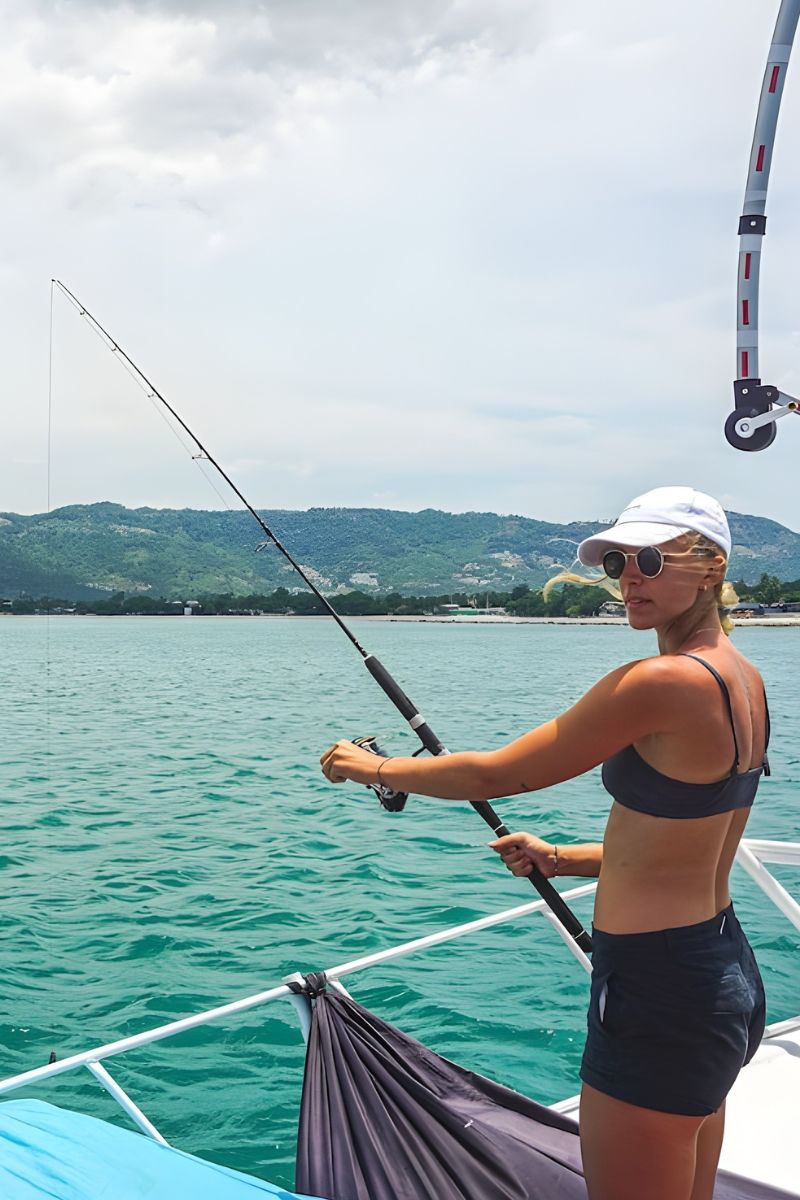 Woman fishing on a boat with mountains in the background