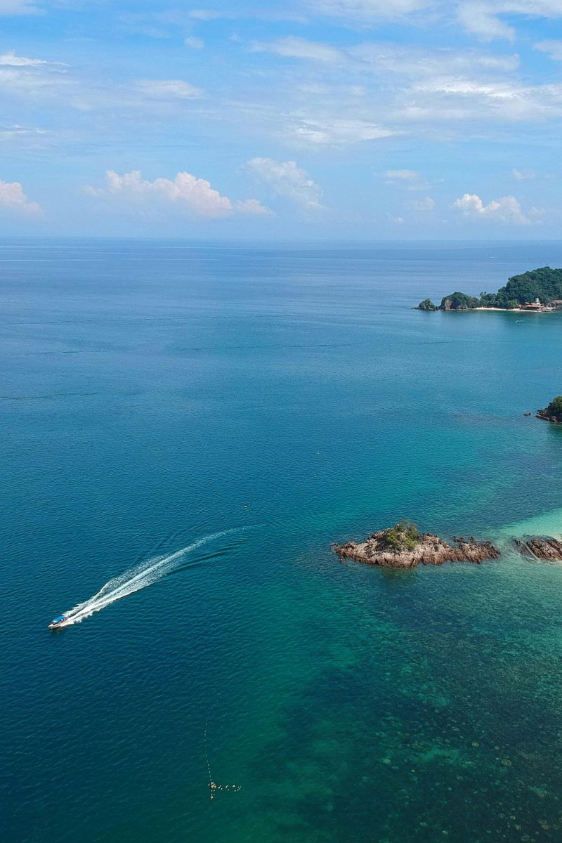 Aerial view of a boat on clear blue water with an island in the distance.