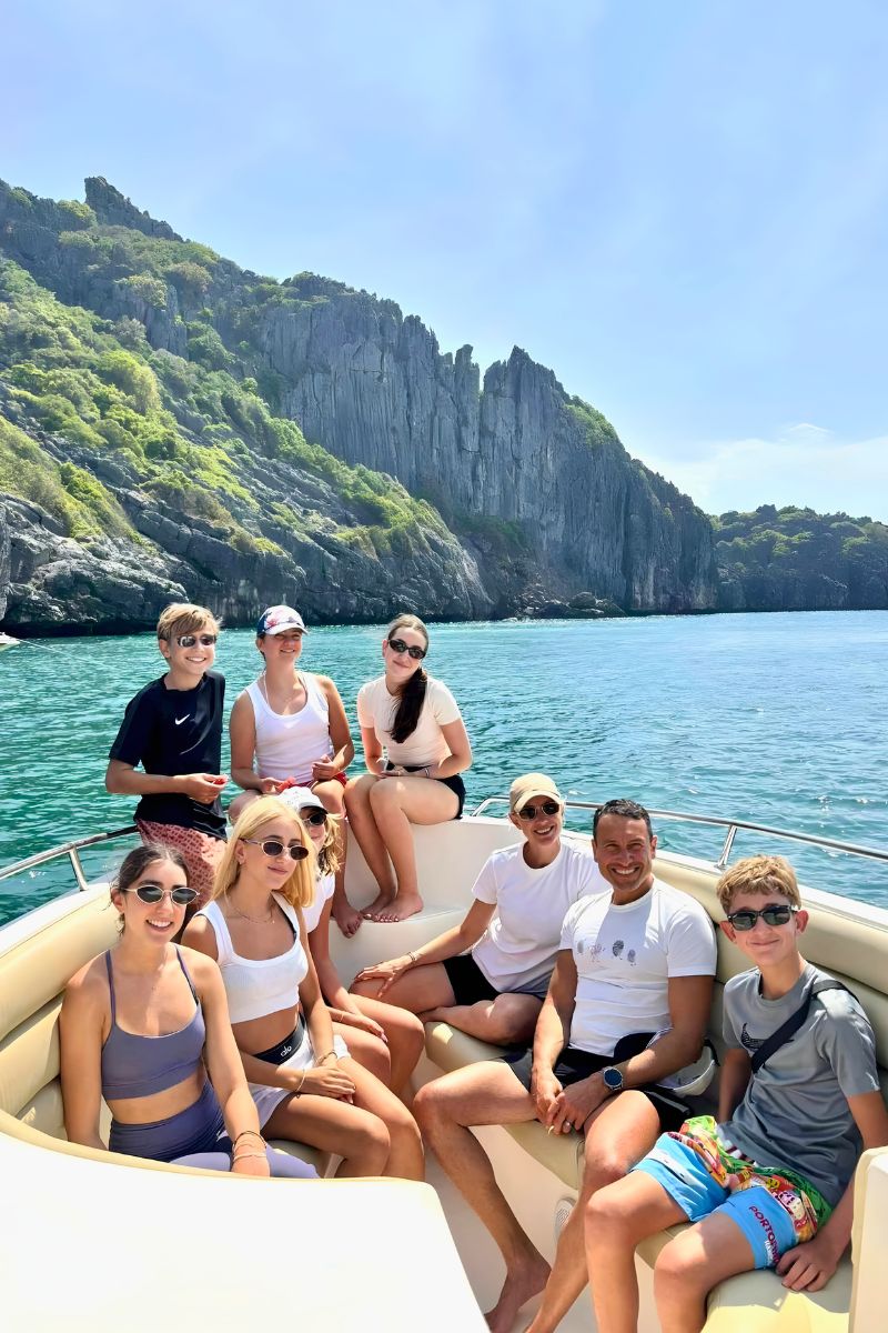 Group of people on a boat with a scenic background of cliffs and water.