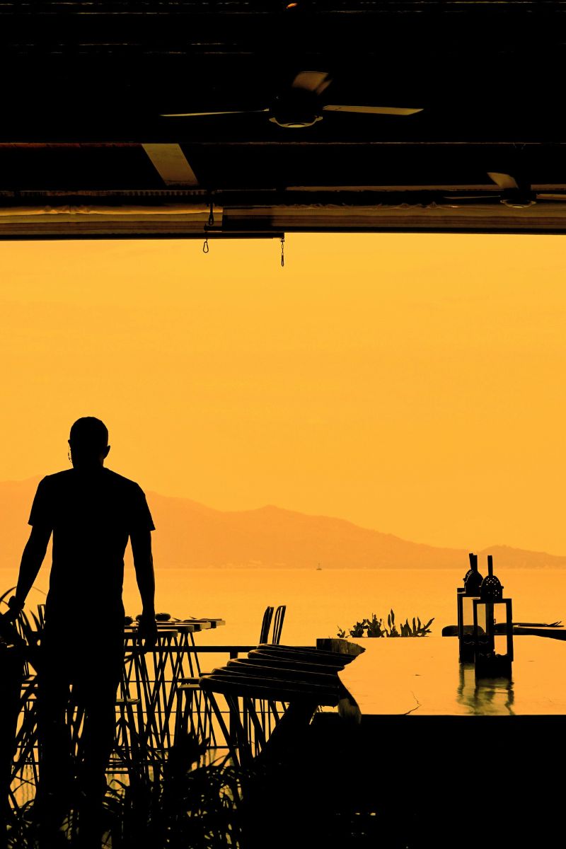 Silhouette of a person standing by a table with bottles against an orange sunset sky.