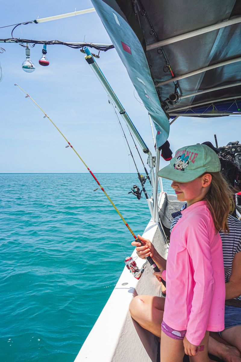 Child fishing on a boat with clear blue water and sky.