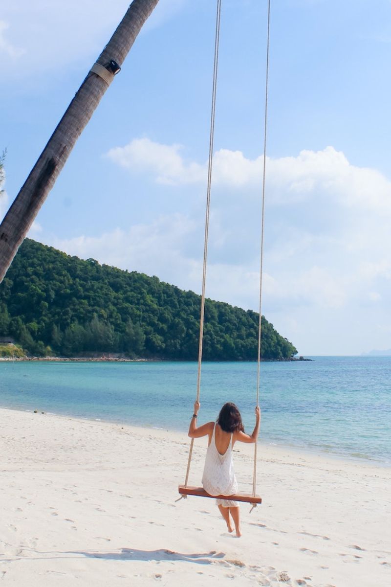 Person on a swing by the beach with a tropical island in the background
