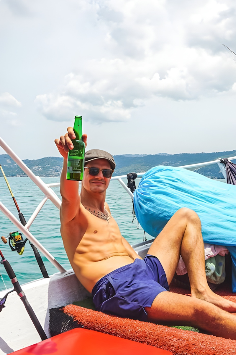 Man on a boat holding a beer bottle with a scenic background