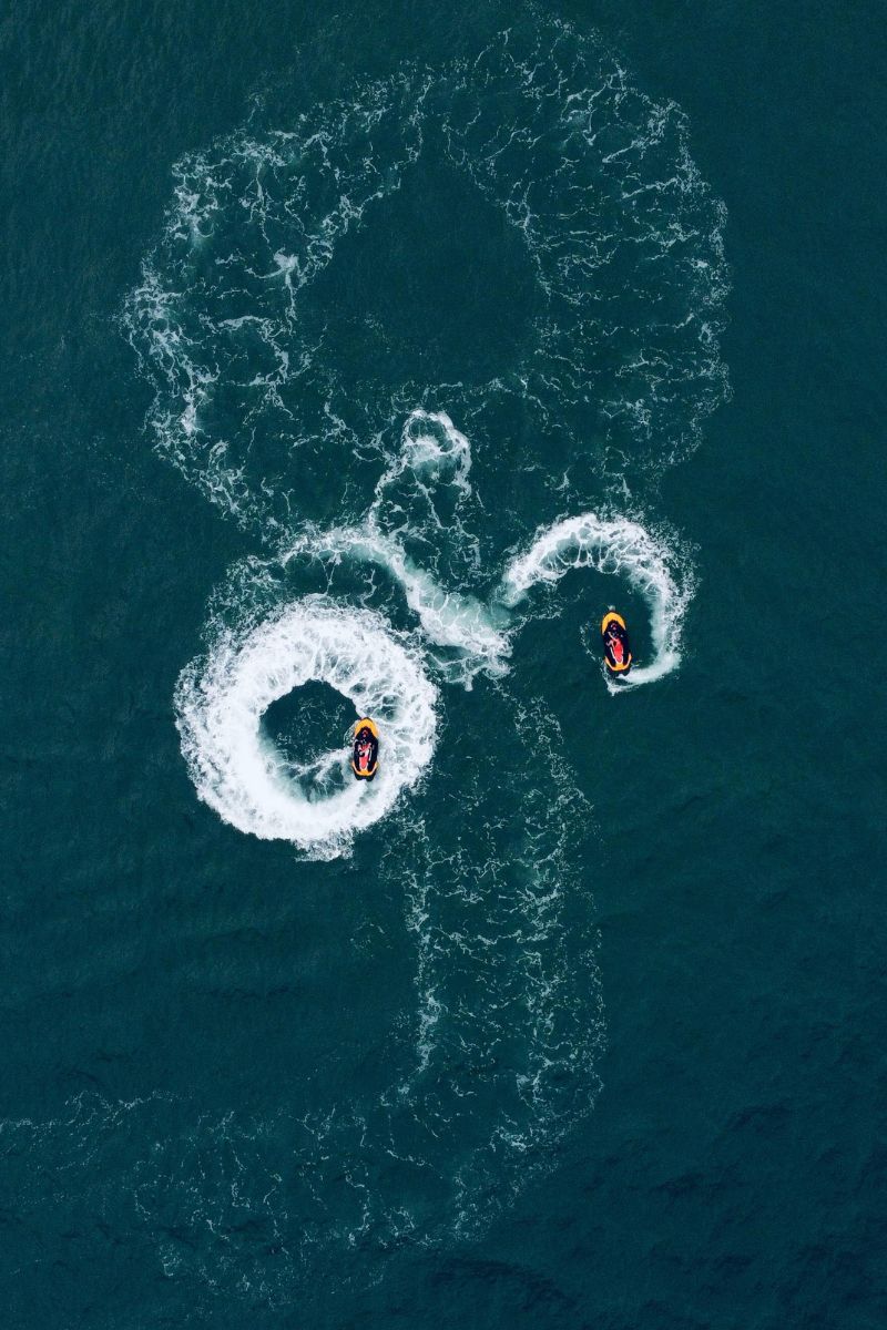 Three people on jet skis creating circular wakes in the water from an aerial perspective.