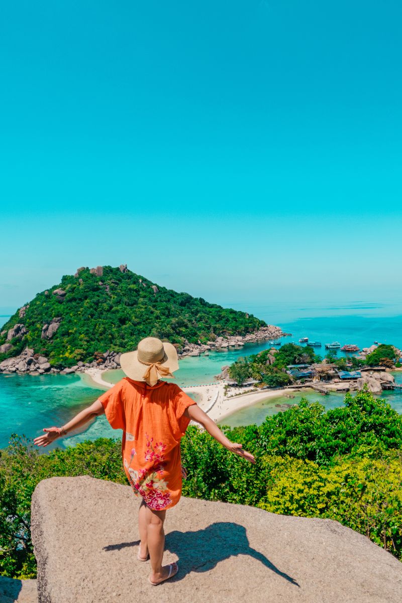 Woman in an orange dress and hat overlooking a tropical island with turquoise waters.