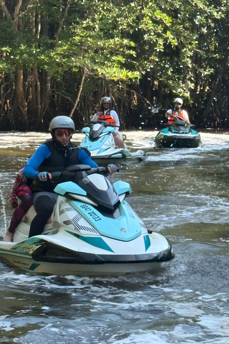 People riding jet skis through a waterway with trees in the background