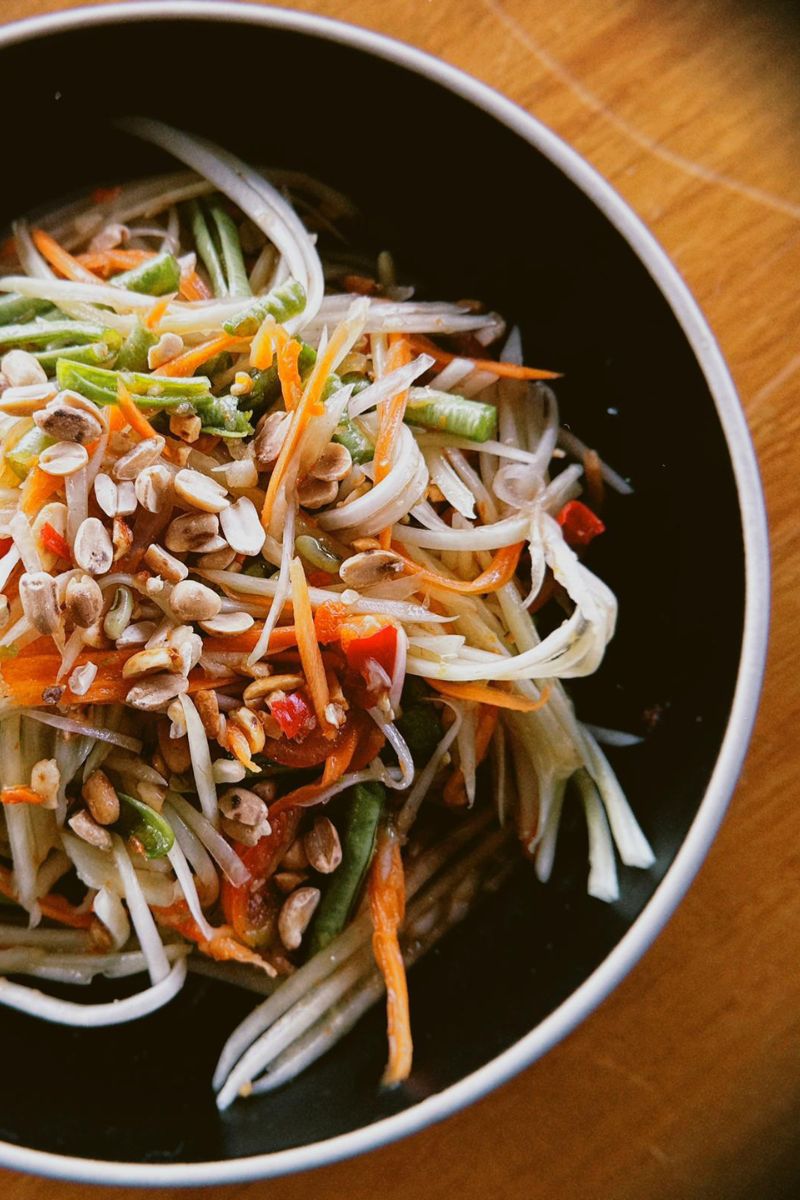 Vegetable salad with noodles and seeds in a black bowl on a wooden table