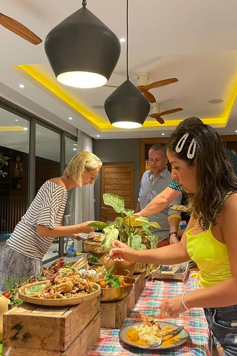 Two women preparing food at a table in a modern kitchen with yellow accent lighting.