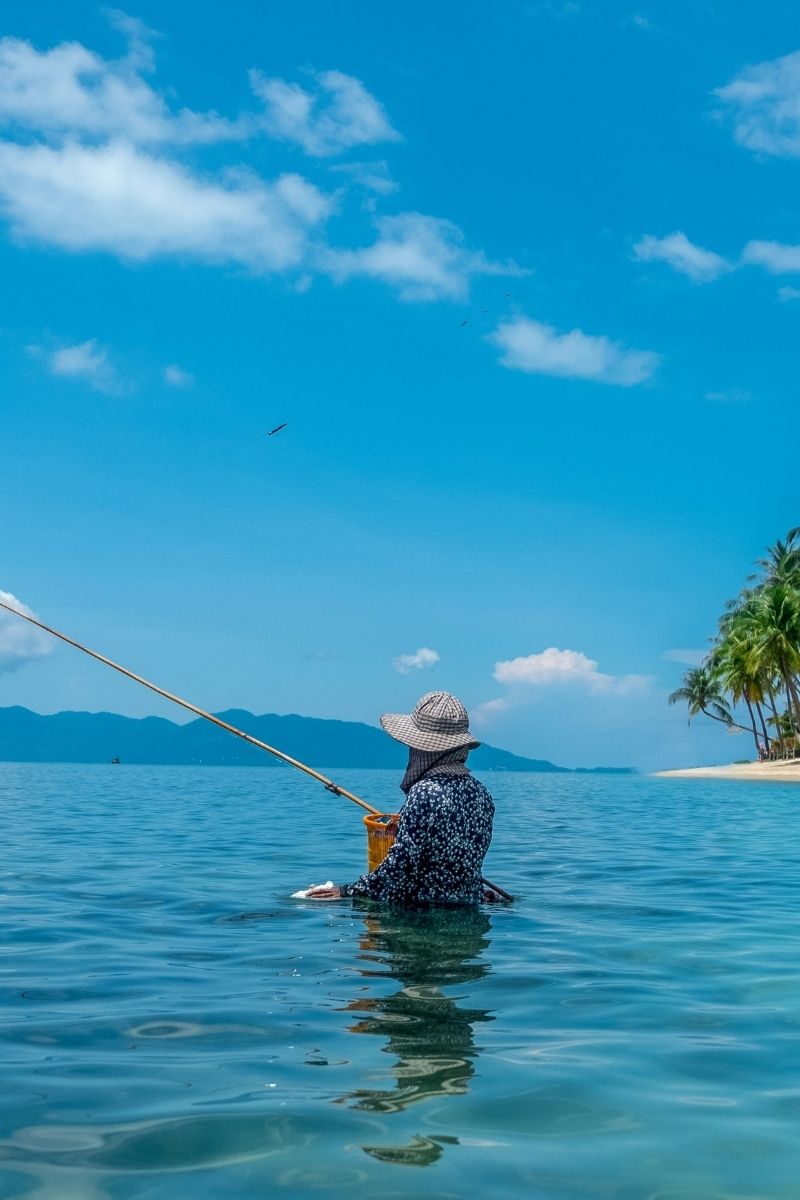Person fishing in the ocean with a clear blue sky and distant island.