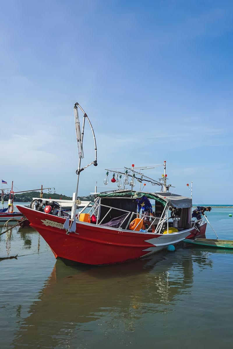Red fishing boat docked at a harbor with clear blue sky