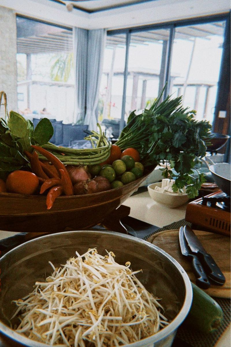 Assorted vegetables including carrots, beans, and leafy greens on a table with a large window in the background.