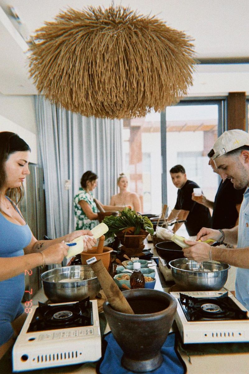 Group of people cooking together in a kitchen with a rustic pendant light.