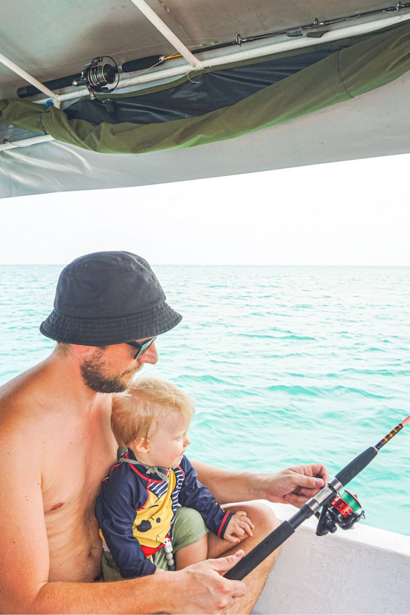 Man and child fishing on a boat with clear water in the background