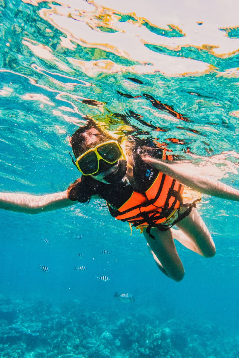 Two people snorkeling in clear blue water with a child wearing an orange life jacket.