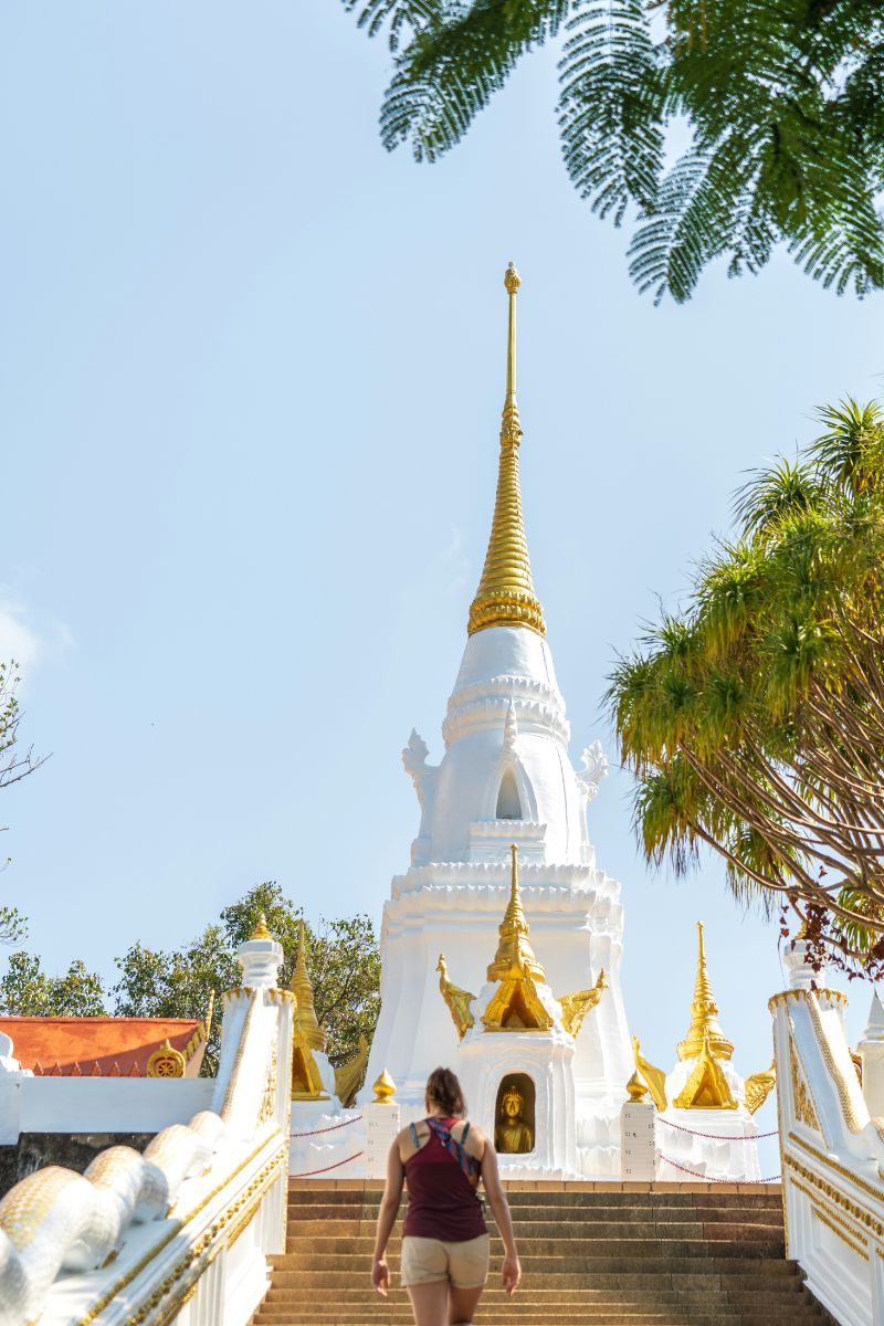 Woman walking towards a white temple with gold accents on a sunny day.