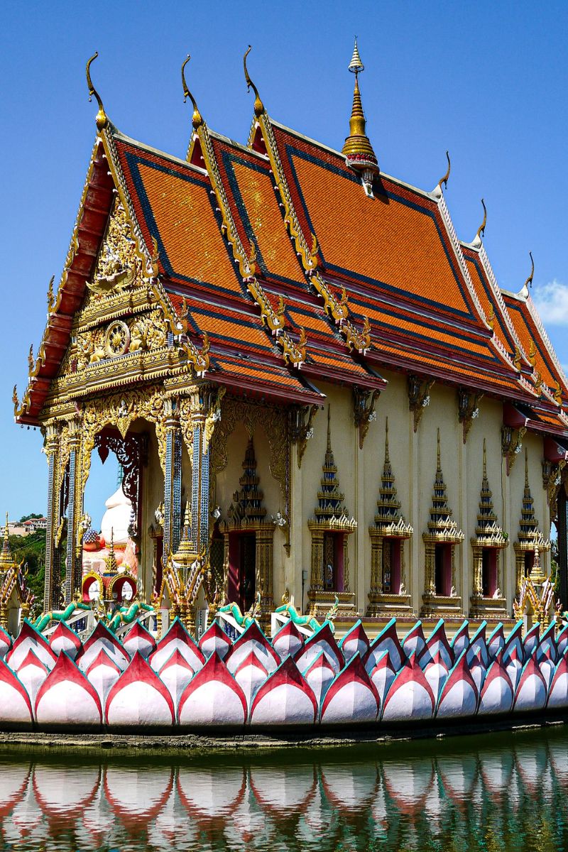 Traditional Thai temple with ornate roof and decorative elements by a body of water.